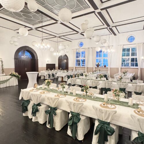 Eleganter, weiß dekorierter Festsaal mit gedecktem Hochzeitstisch.