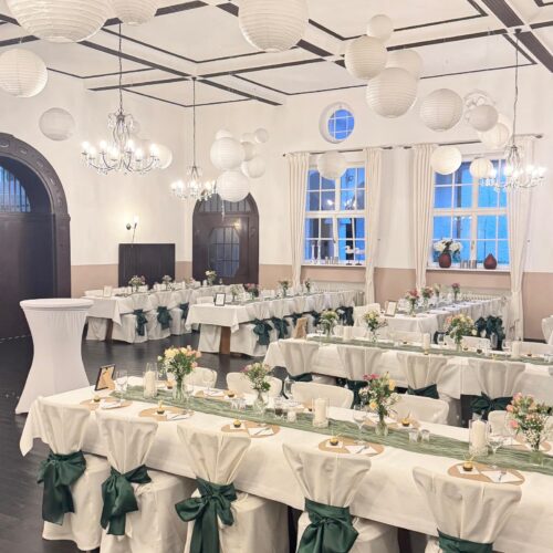 Eleganter Hochzeitssaal, weiße Tischdecken, grüne Schleifen, Papierlampions.