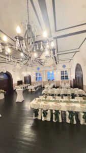 Eleganter Festsaal mit Kristallleuchtern, gedeckten Tischen und grünen Schleifen.