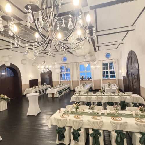 Eleganter Festsaal mit Kristallleuchtern, gedeckten Tischen und grünen Schleifen.