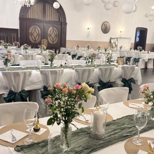 Festlich dekorierter Speisesaal mit langen, weiß eingedeckten Tischen.